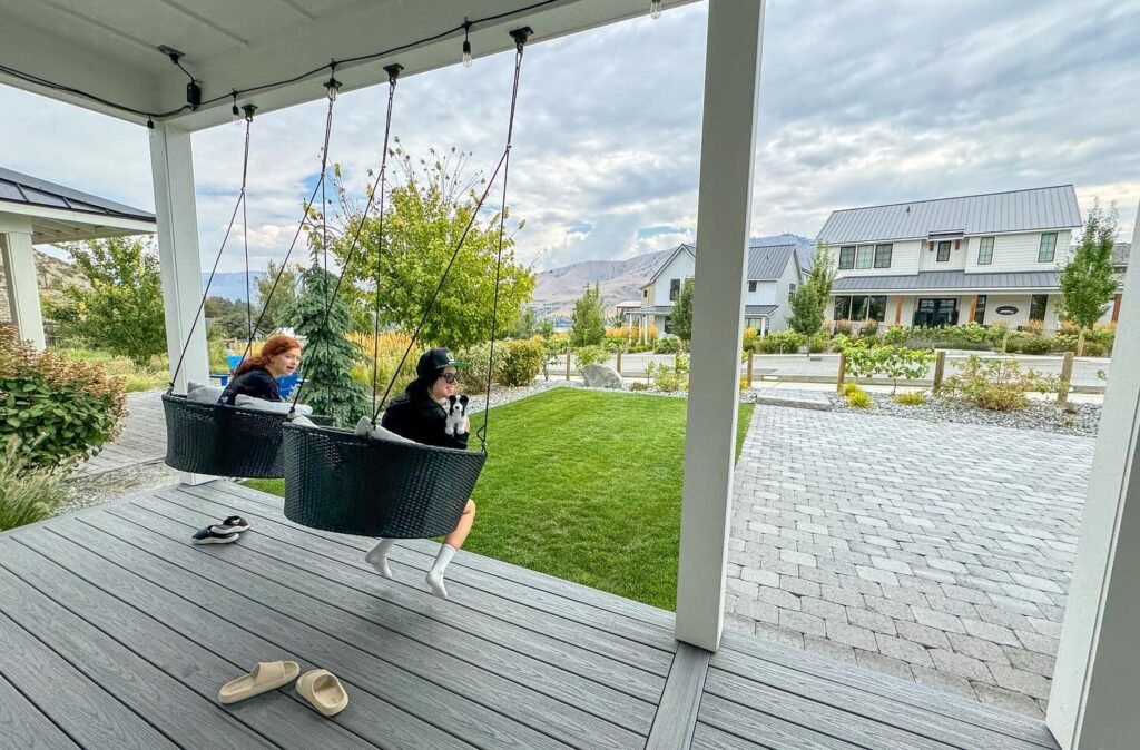 A covered deck with hanging swing seats offers a relaxed setting overlooking a modern house.