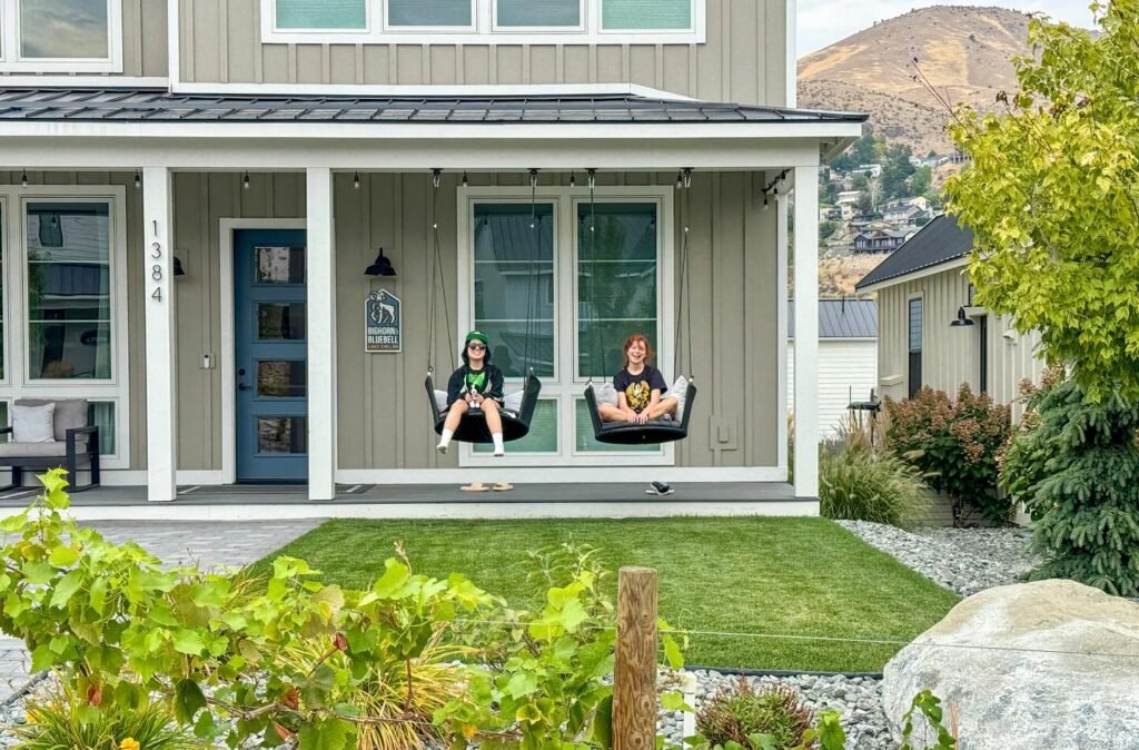 Two people are seen sitting on a porch swing, enjoying a beautiful view of green mountains and a new home.