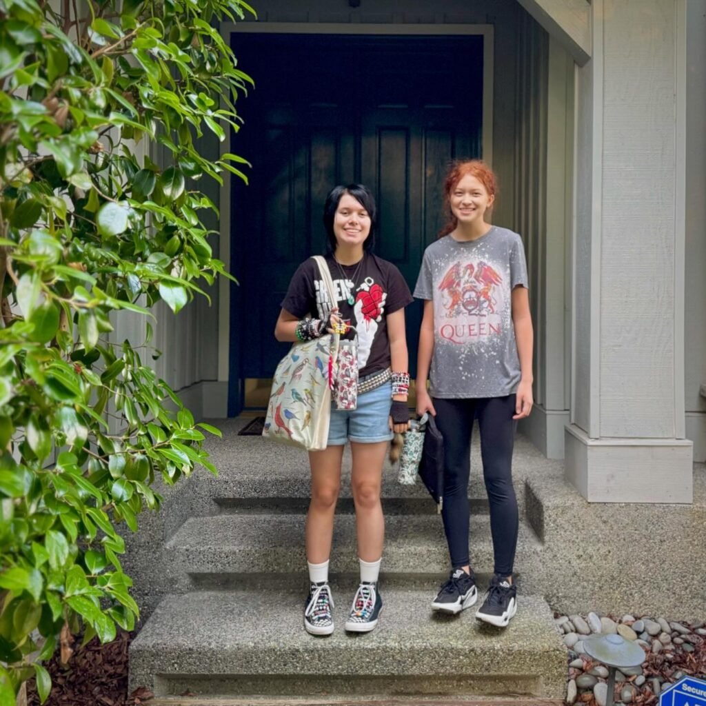 Two visitors stand on stone steps in front of a museum entrance in Seattle. Green foliage frames the scene beside a classic building facade.