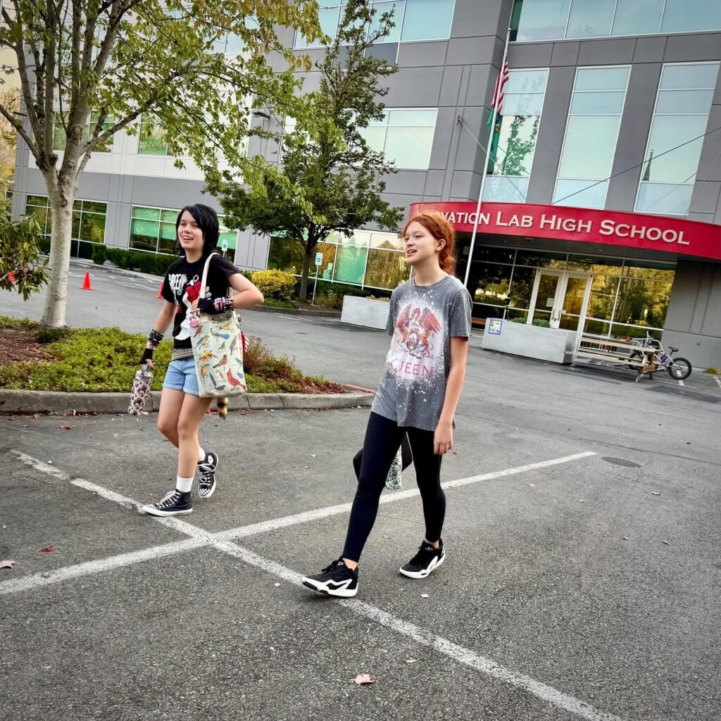 Two people stand in the parking lot of North Capitol Lab High School during the day. The modern glass building is visible in the background.