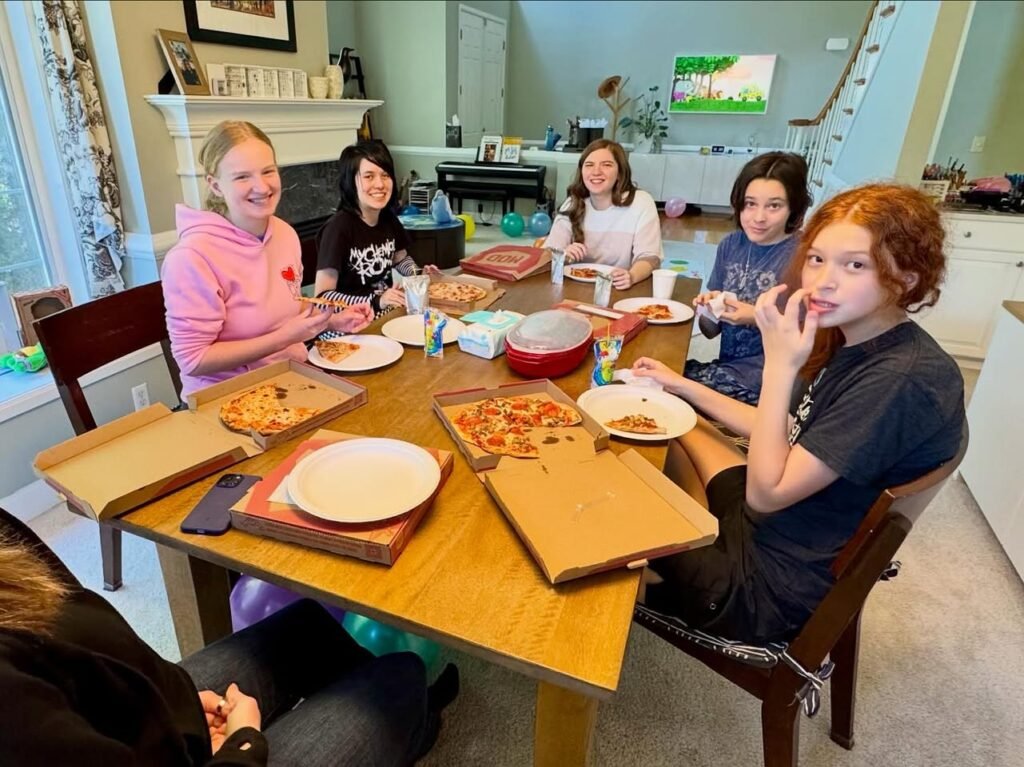 A group of people enjoying a pizza dinner together around a wooden dining table in a cozy home setting.
