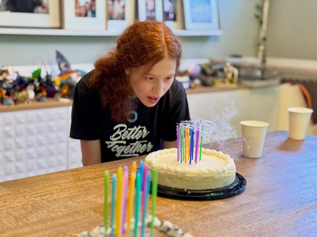 A person blows out colorful candles on a birthday cake at a kitchen table.