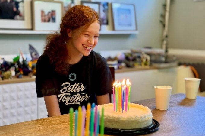 A birthday cake with lit candles and colorful decorations on a wooden kitchen counter