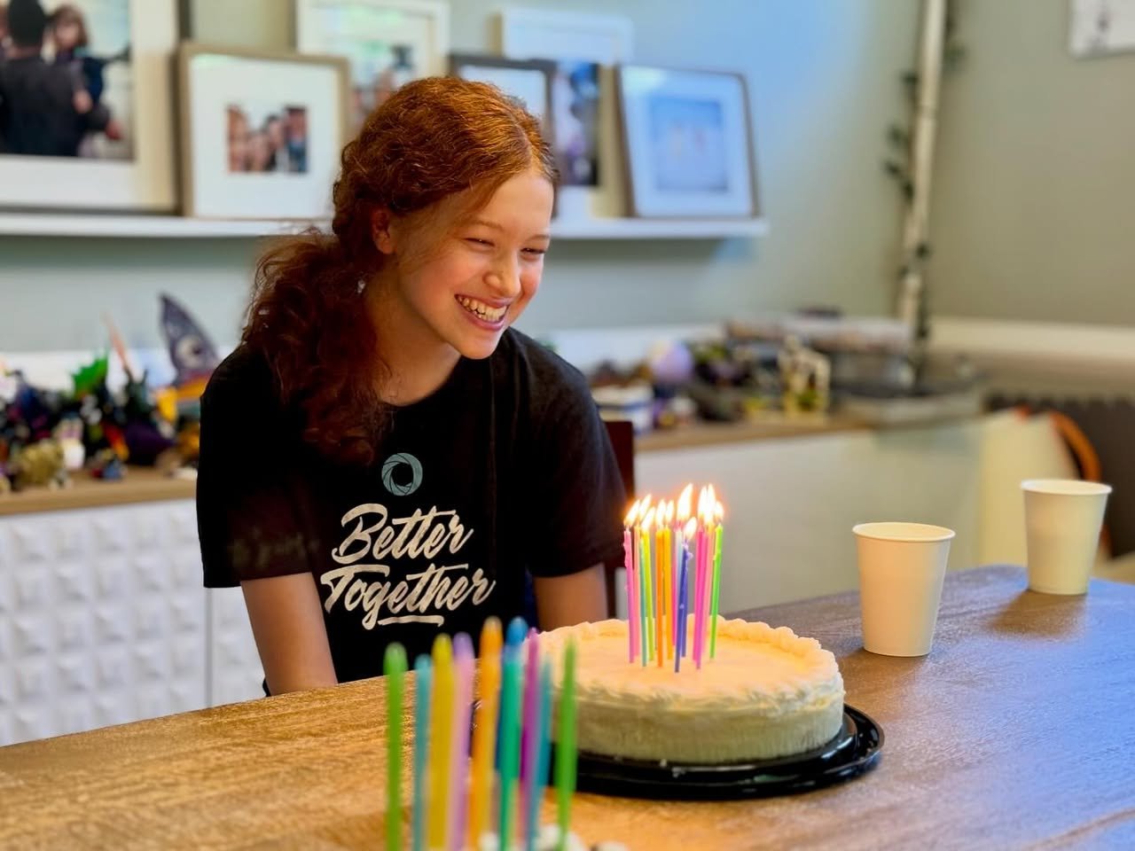 The Twins Turn 15 A birthday cake with lit candles and colorful decorations on a wooden kitchen counter