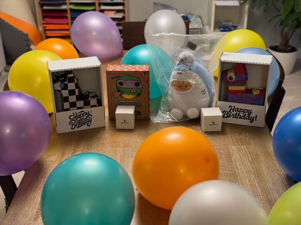 An array of colorful balloons and unique birthday gift boxes on a wooden table indoors.