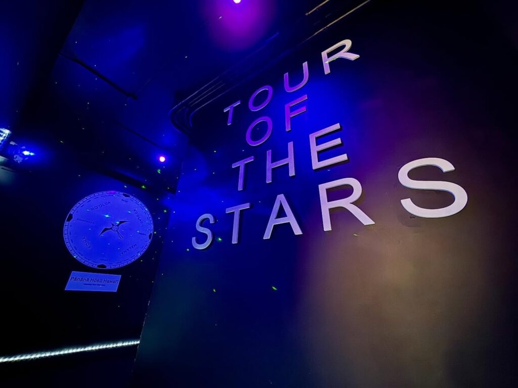 Illuminated sign reading Tour of the Stars in a dark, blue-lit room. Vibrant purple and blue lighting accents the display.