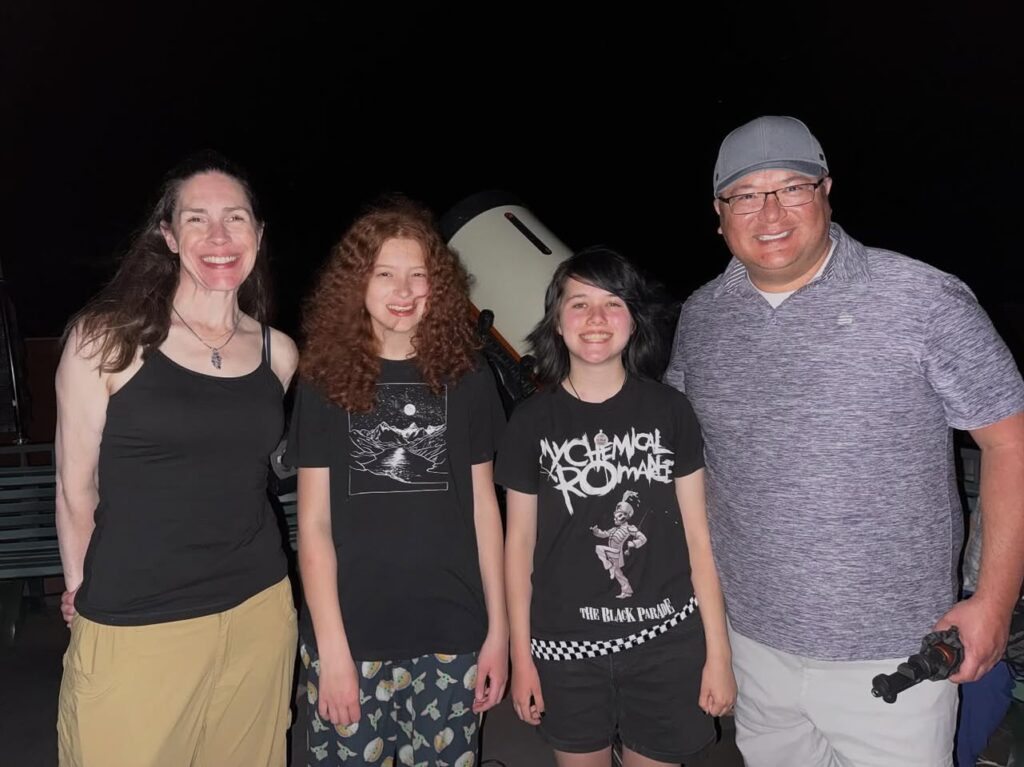People gathered around a telescope under the night sky, capturing a casual stargazing evening.