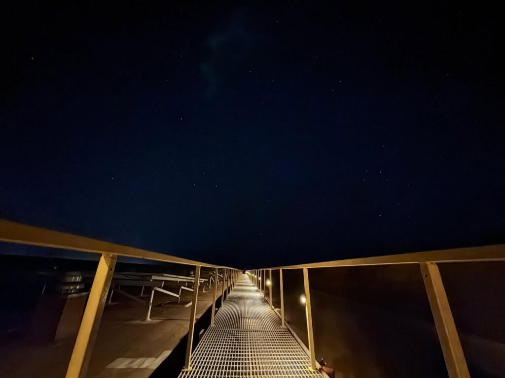 A metal grating walkway with golden railings stretches into the distance under a dark blue night sky ahead.
