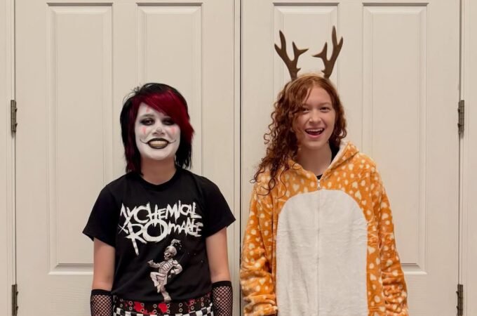 Two costumed family members standing together in front of a white interior door. One wears a punk rock outfit with face paint, and the other a reindeer onesie.