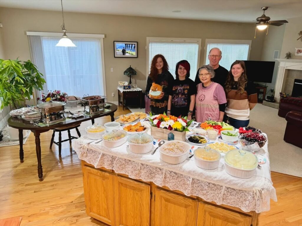 A group of people poses behind a kitchen island filled with food and drinks in a bright home.