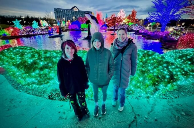 A family enjoys visiting a vibrant holiday light show. The festive atmosphere is highlighted by colorful LEDs and glowing trees.