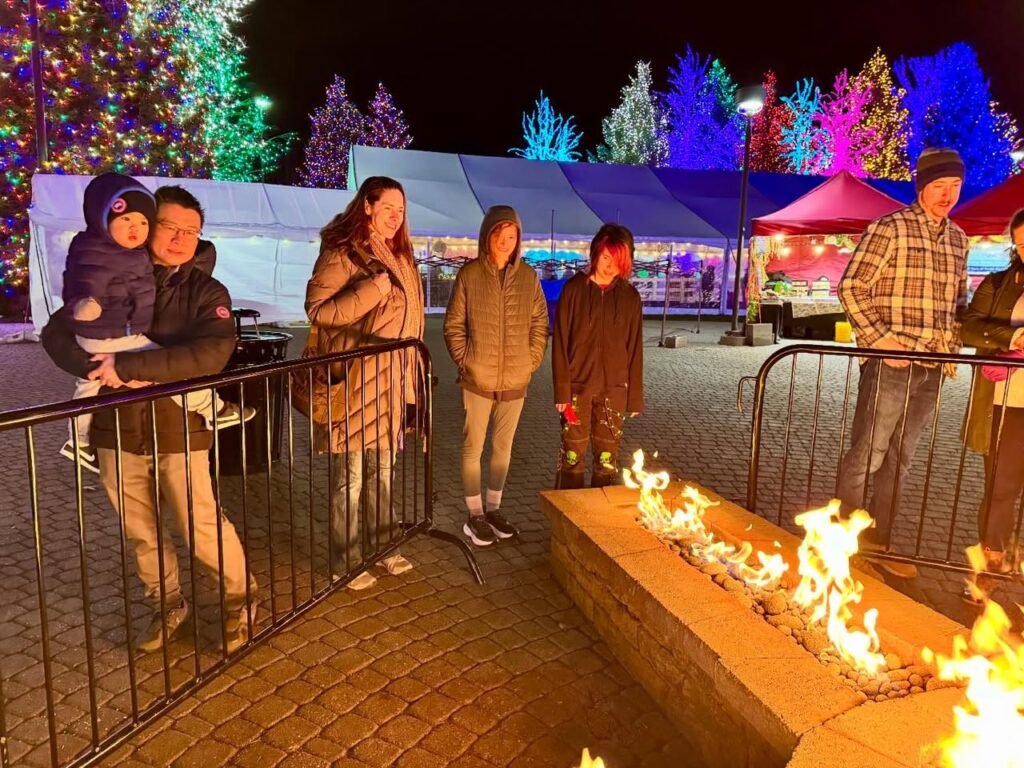 Family enjoying a festive night with glowing holiday trees and a warm fire pit.