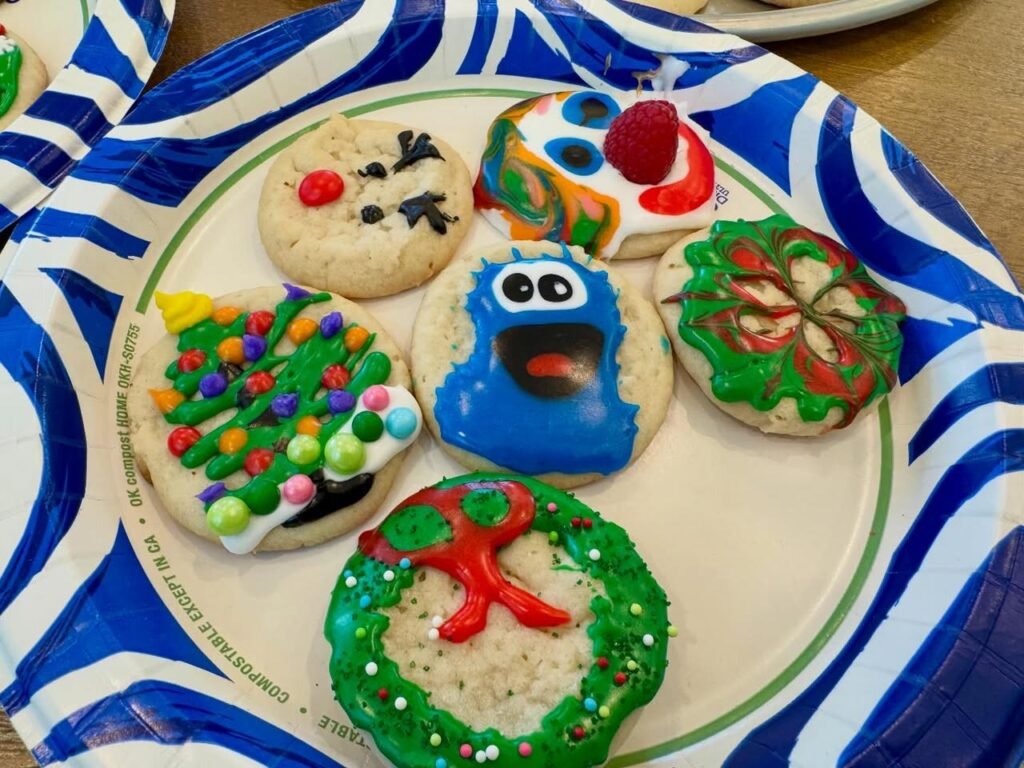 Colorful frosted sugar cookies featuring snowmen, wreaths, and characters on striped blue plates.