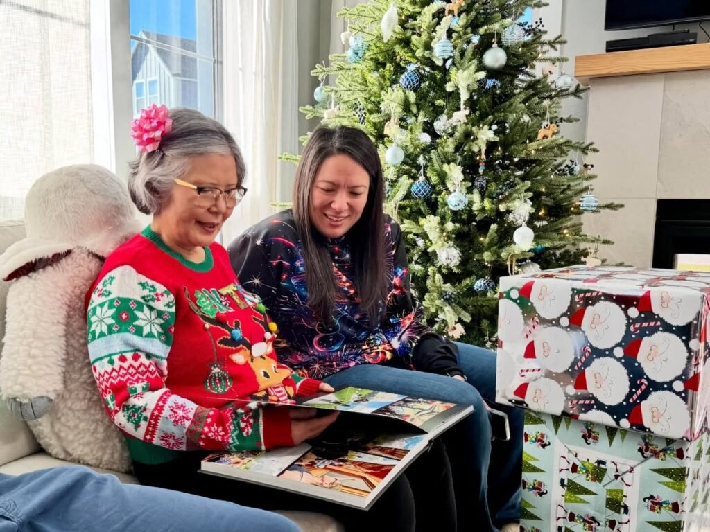 Two people looking at a photo album by a Christmas tree.