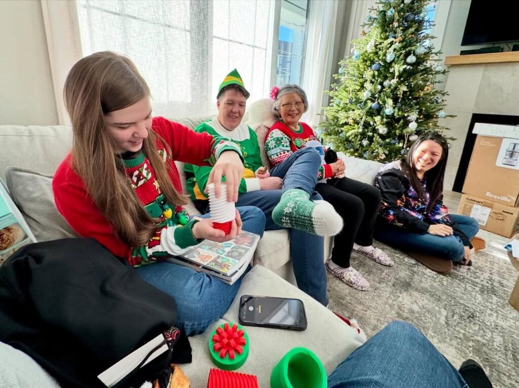 A family enjoys a festive Christmas gathering in a cozy living room, wearing holiday-themed sweaters near a decorated tree.
