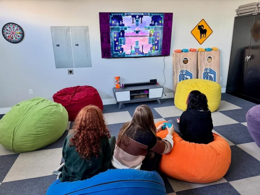Friends sitting on colorful bean bags while playing a video game in a basement living room.