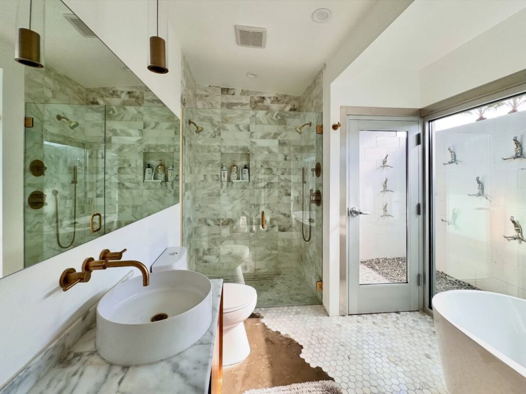 A spacious bathroom featuring a white vessel sink, marble countertops, and a glass-enclosed shower.