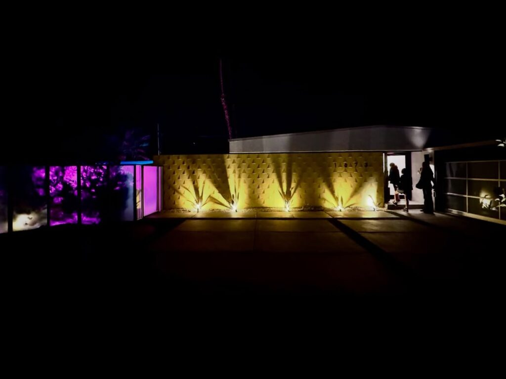A nighttime shot of a stage area with dramatic purple and yellow lighting. The scene includes silhouetted figures near a railing.