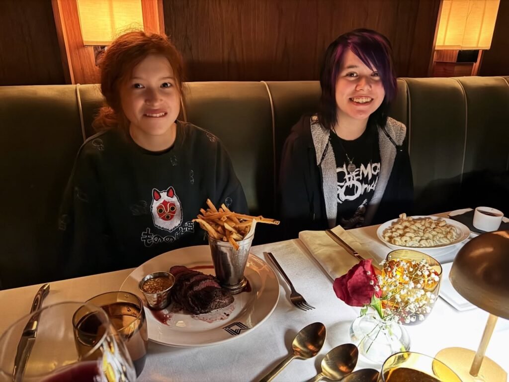 A family enjoys a meal together at a cozy restaurant booth with warm lighting, featuring a dessert and a glass of juice.