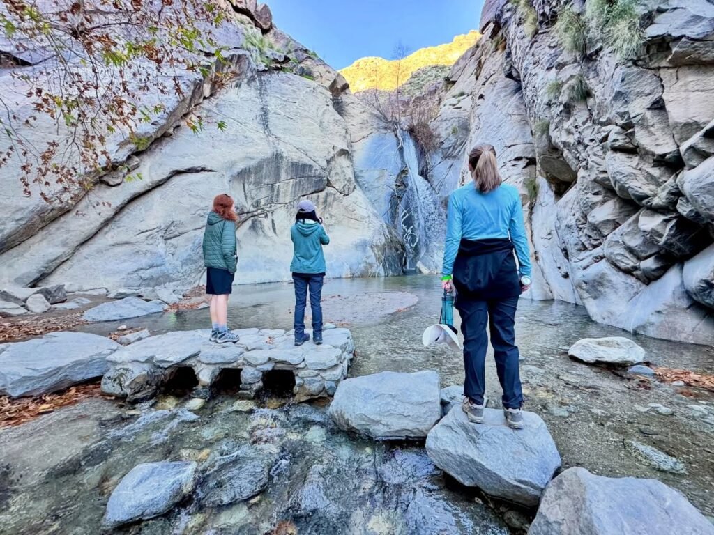 Visitors exploring a rocky landscape with a waterfall in the background, enjoying a rugged hiking experience.