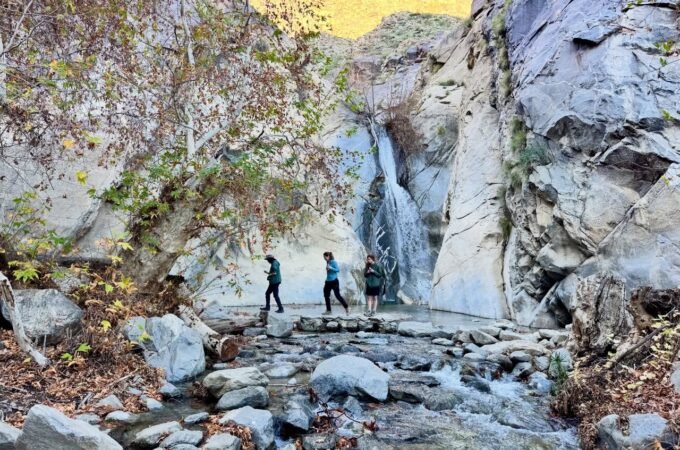 A scenic view of a waterfall cascading down a rocky cliff with hikers at its base.