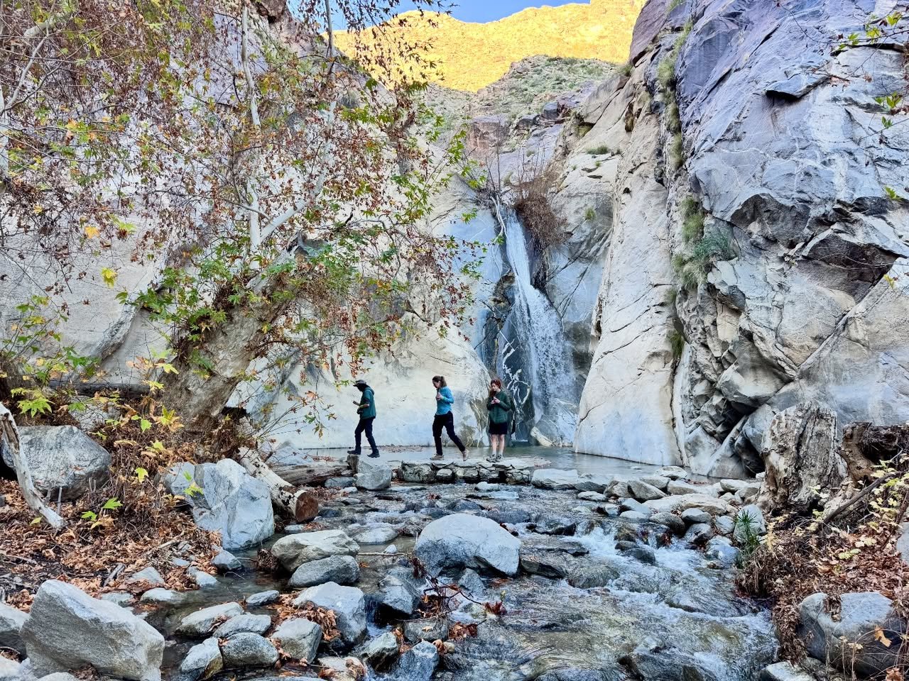A scenic view of a waterfall cascading down a rocky cliff with hikers at its base.