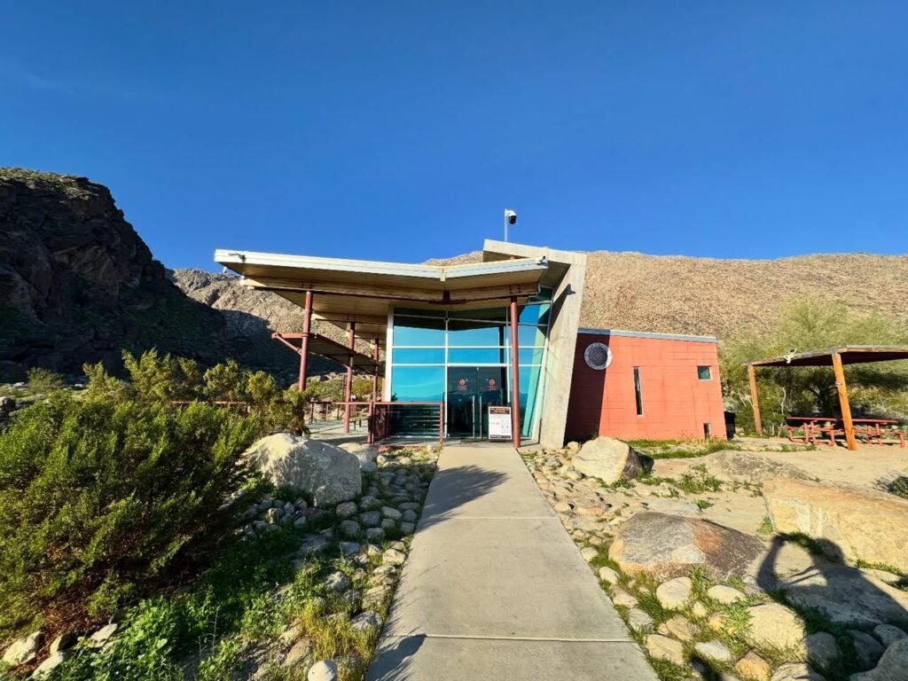 A modern building with colorful glass doors sits nestled among desert hills under a clear blue sky.