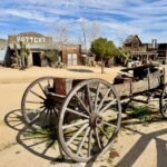 Andreas Canyon A rustic wooden wagon sits in a dusty street in front of the antique western building labeled Pottery.