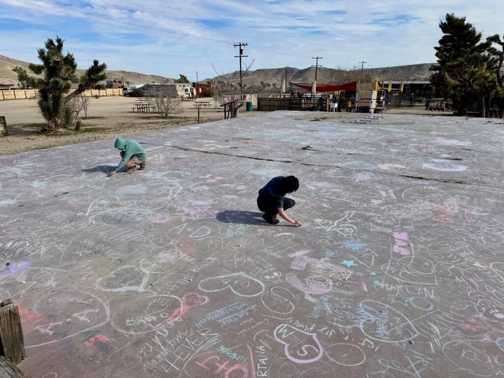People creating large colorful chalk drawings on a concrete playground in a desert town.