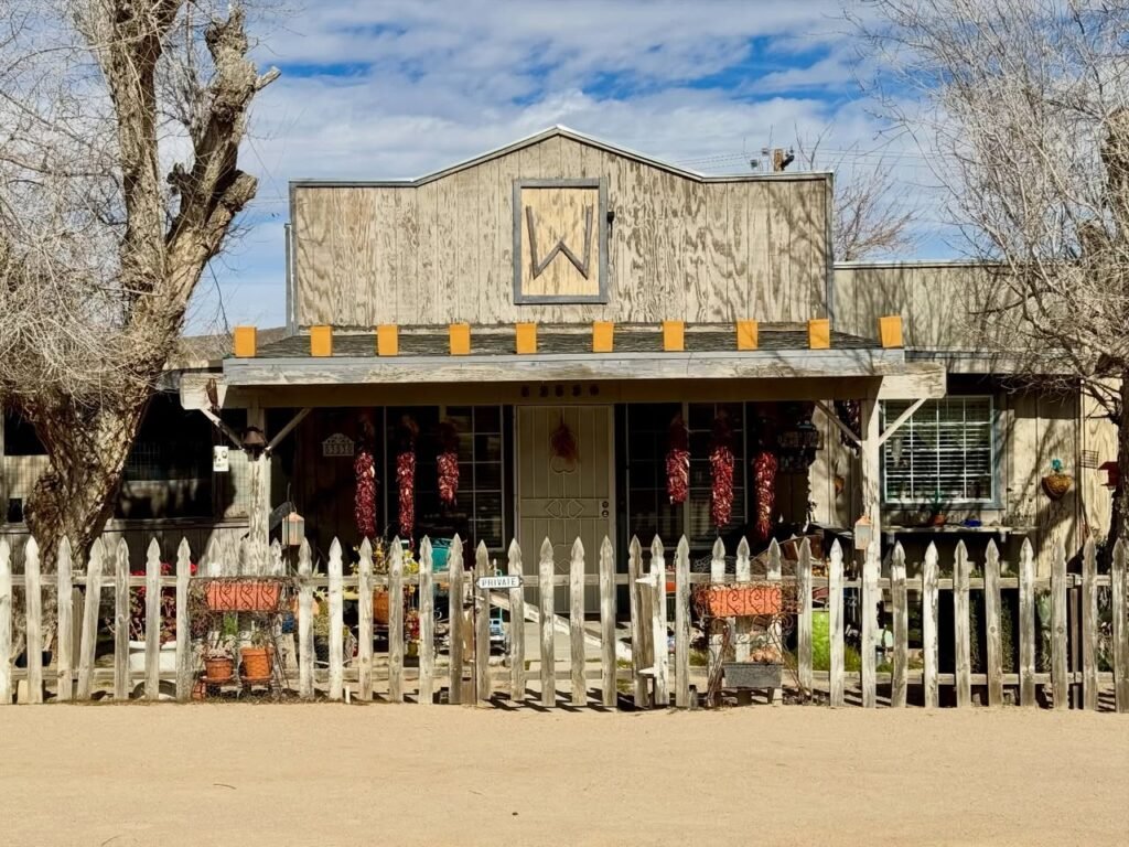 A restored Old West jailhouse with a white picket fence and rustic decor situated in a desert landscape.