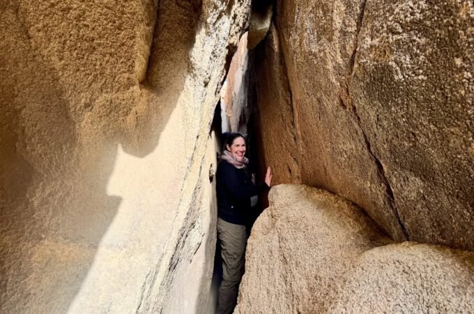 A person navigating a narrow gap between massive rock formations, highlighting the scale of the landscape.