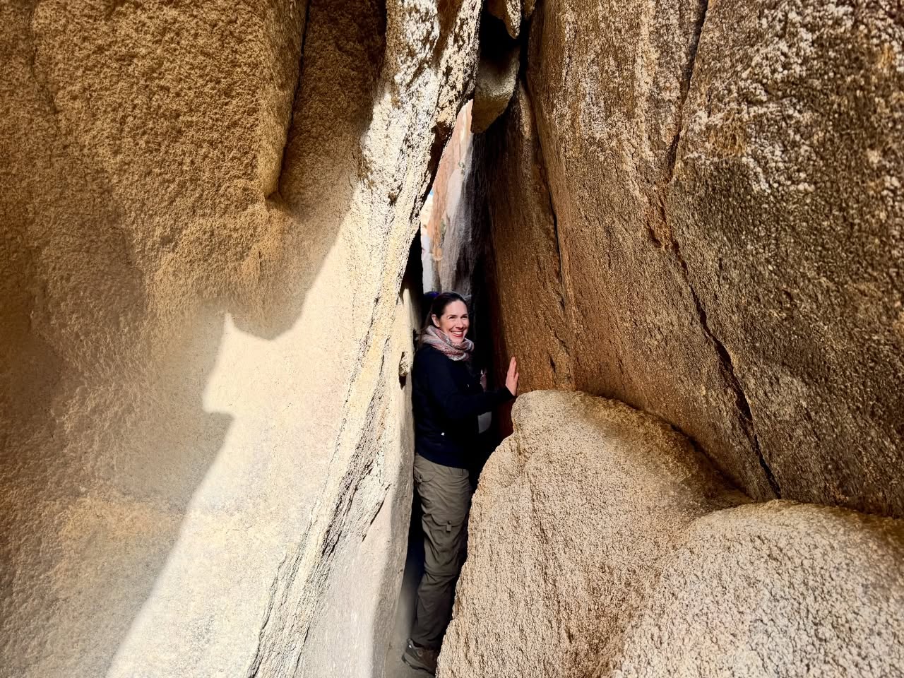 A person navigating a narrow gap between massive rock formations, highlighting the scale of the landscape.