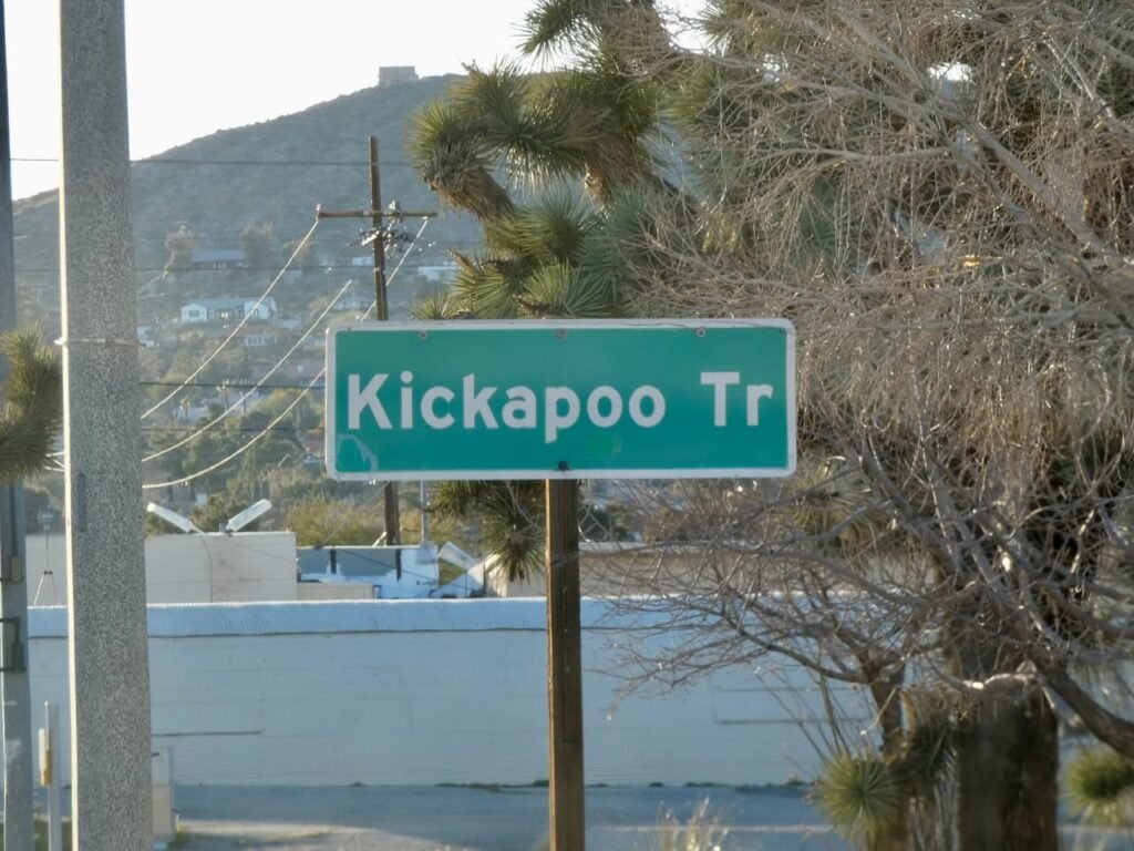 Green street sign for Kickapoo Trail framed by trees and hills in the Pacific Northwest.