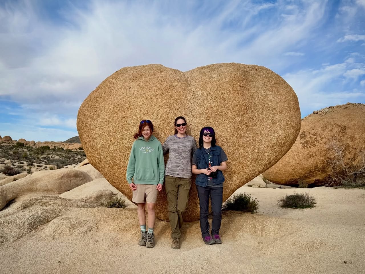 Heart Rock A group of three travelers posing in front of a massive heart-shaped boulder in a desert landscape.