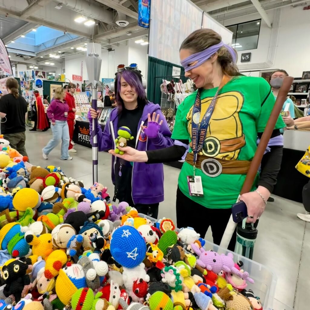Two people in costumes explore a colorful pile of stuffed animals at a convention.