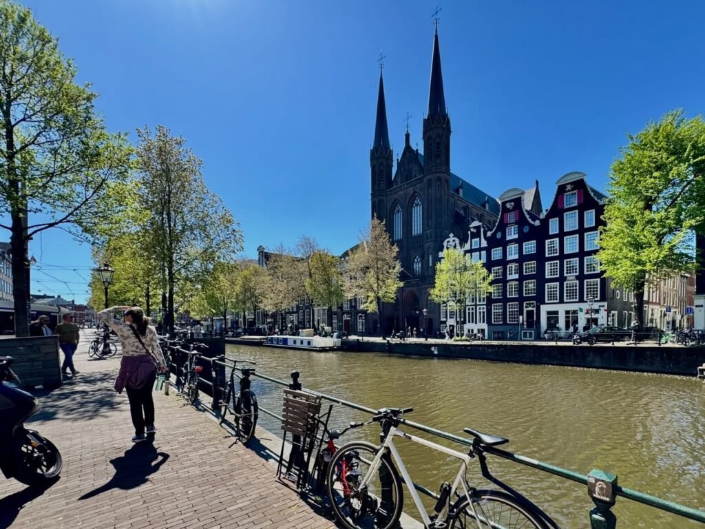 Amsterdam canal side with bicycles and historic churches under a clear blue sky.