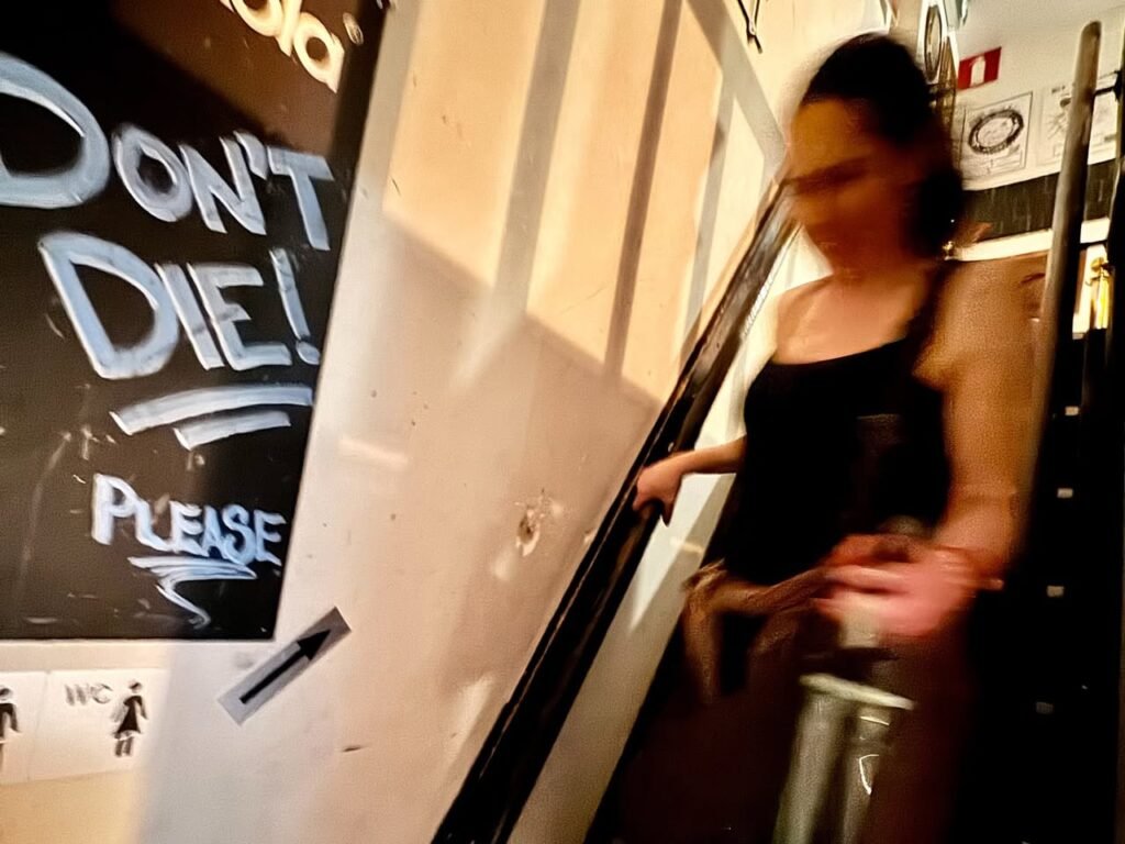 A close-up of a wall sign reading Don't Die! Please with a person standing beside it in an indoor setting.