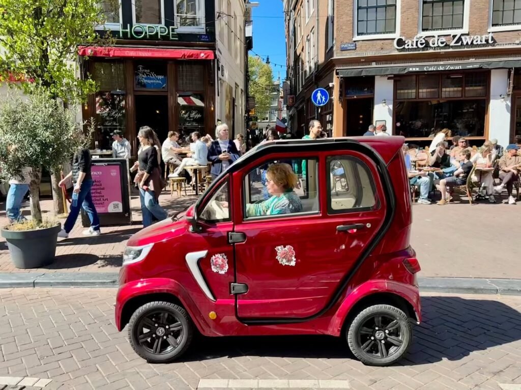 A small red compact car parked on a European city street in front of cafes.