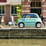 Eating Amsterdam A mint green car parked along a historic canal in Europe. Pedestrians walk past charming brick buildings with red shutters.