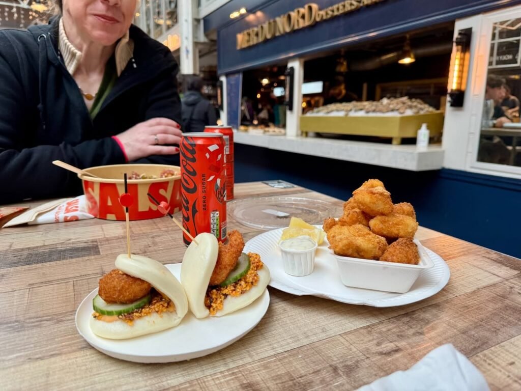A person dining at a street food stall in the Pacific Northwest, enjoying buns with meatballs and a side of fried snacks.