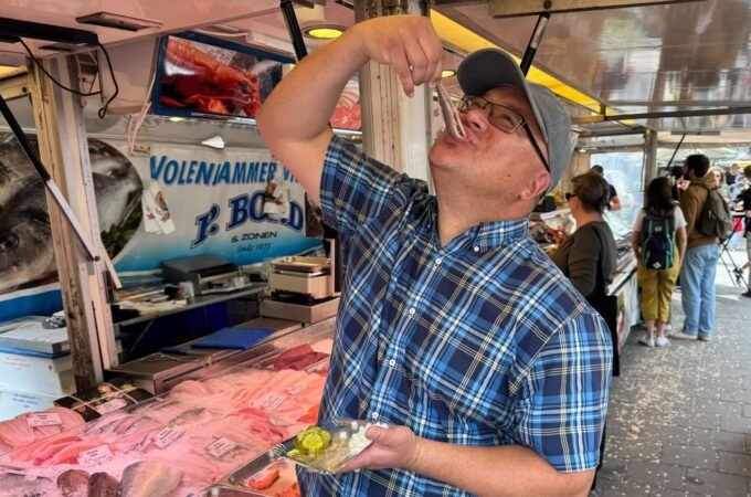 A close-up of a person enjoying fresh seafood with a fork at the floating fish market in Amsterdam.