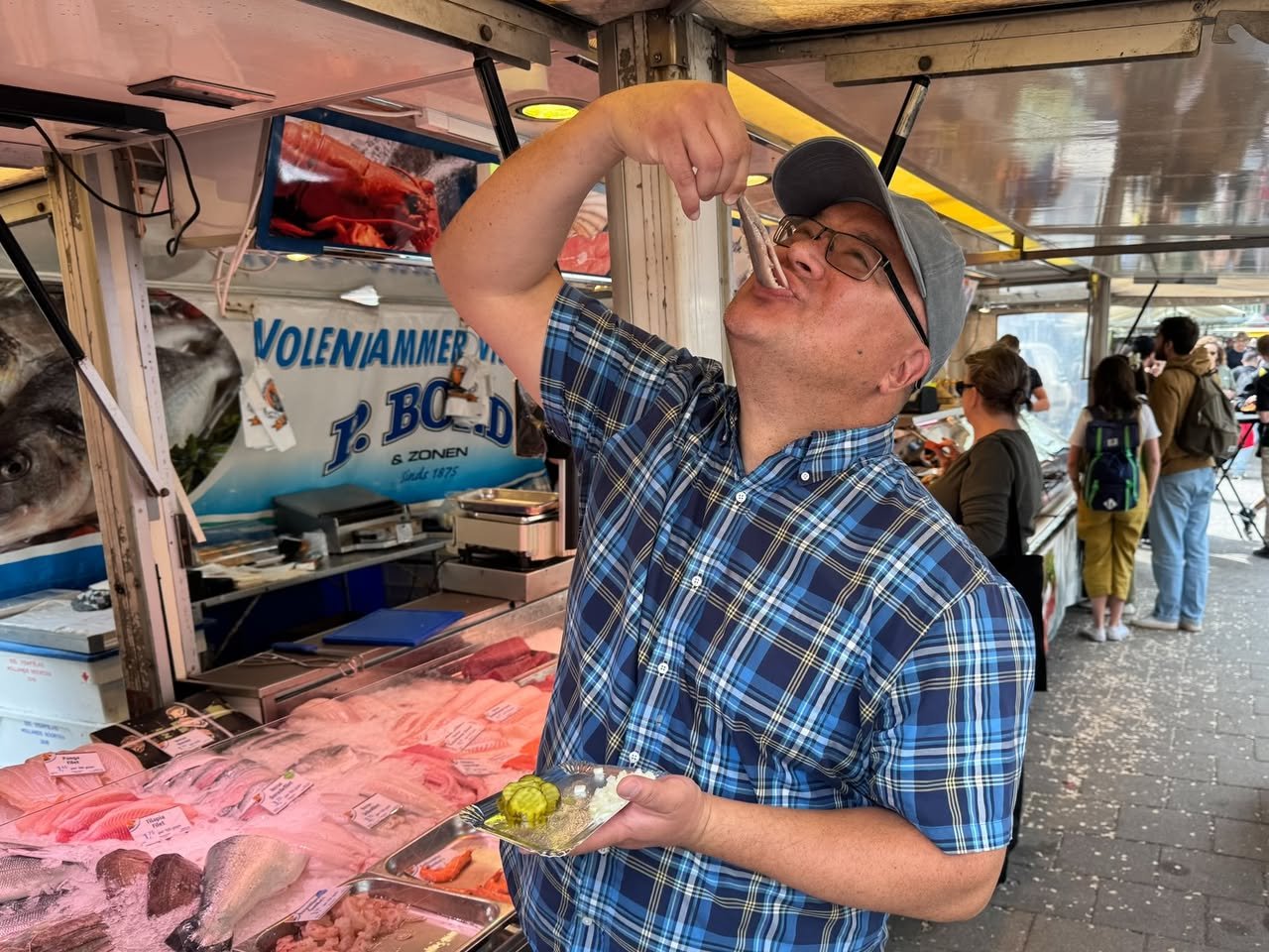 Eating Amsterdam A close-up of a person enjoying fresh seafood with a fork at the floating fish market in Amsterdam.