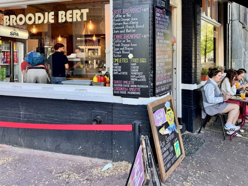 The exterior of Broodje Bert, a quirky café in Amsterdam with a chalkboard menu and sidewalk seating.