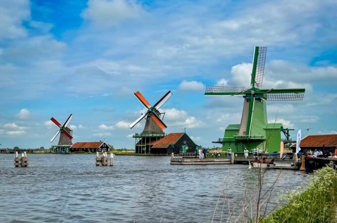 Traditional Dutch windmills with their sails catching the wind, set along a calm waterway under a vibrant blue sky.