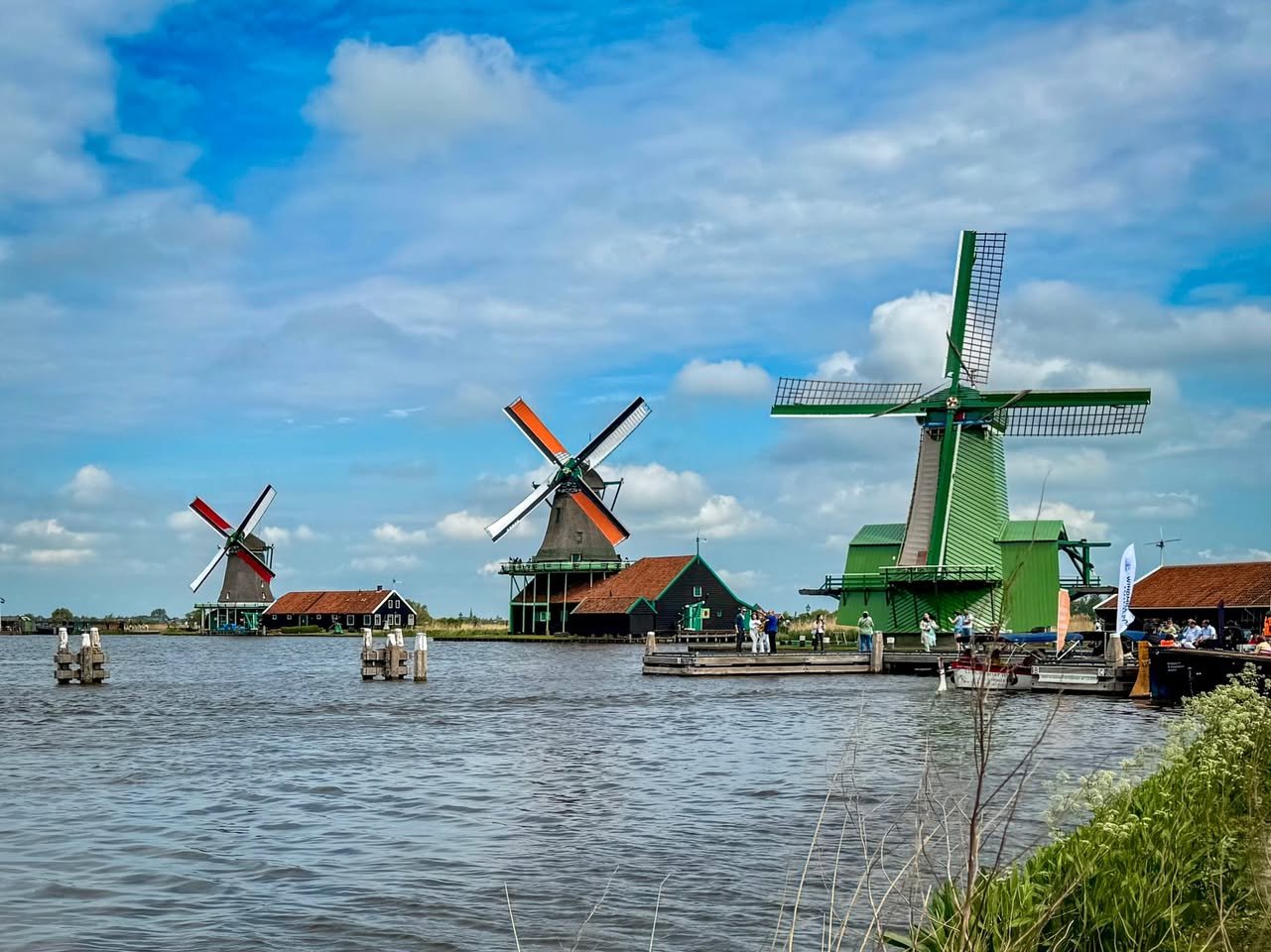 Zaanse Schans Traditional Dutch windmills with their sails catching the wind, set along a calm waterway under a vibrant blue sky.