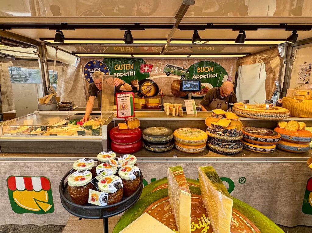 A stall display features an assortment of artisan wheels and wedges of aged cheese.