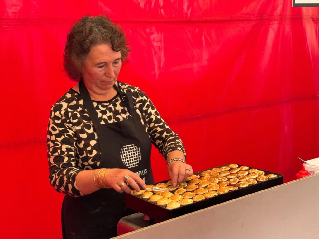 A person is topping freshly baked scones on a tray. The background is a bright red color.
