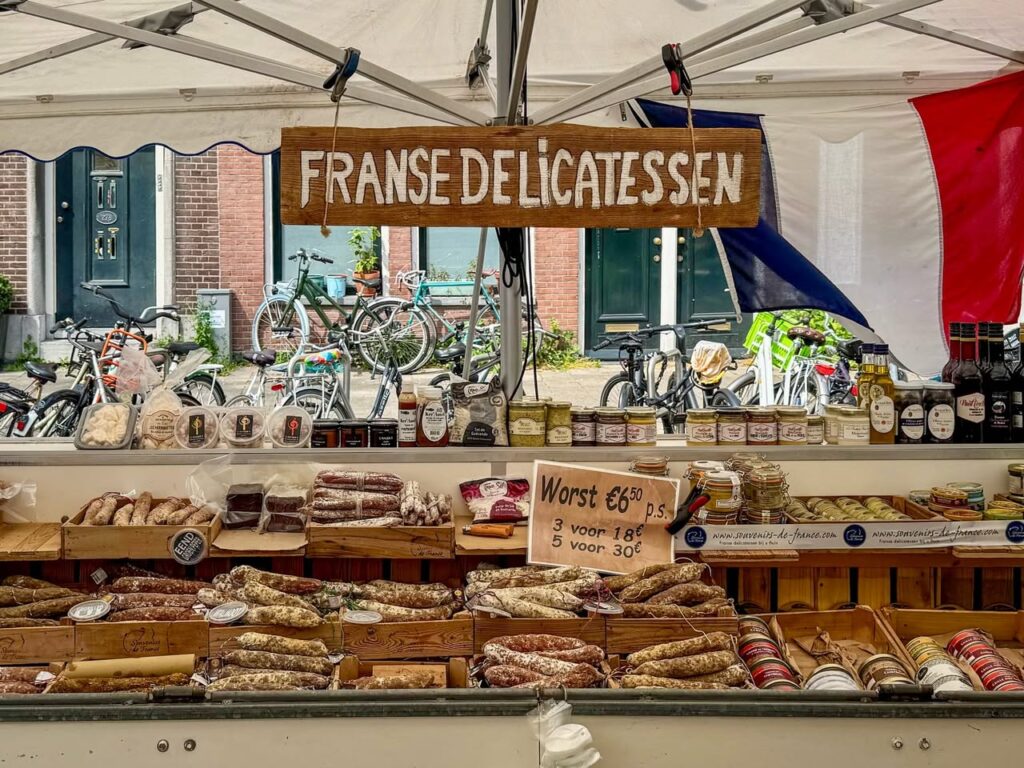 A view of a French Delicatessen market stall displaying various cheeses and meats under a tent.