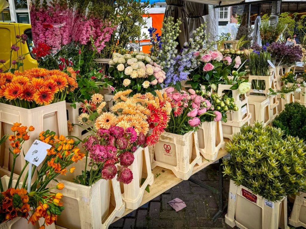 Vibrant flowers, including orange gerberas and pink hydrangeas, displayed in wooden crates at the Amsterdam Flower Market.