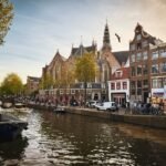 A serene Amsterdam canal lined with historic buildings and a church, framed by trees under a clear sky.